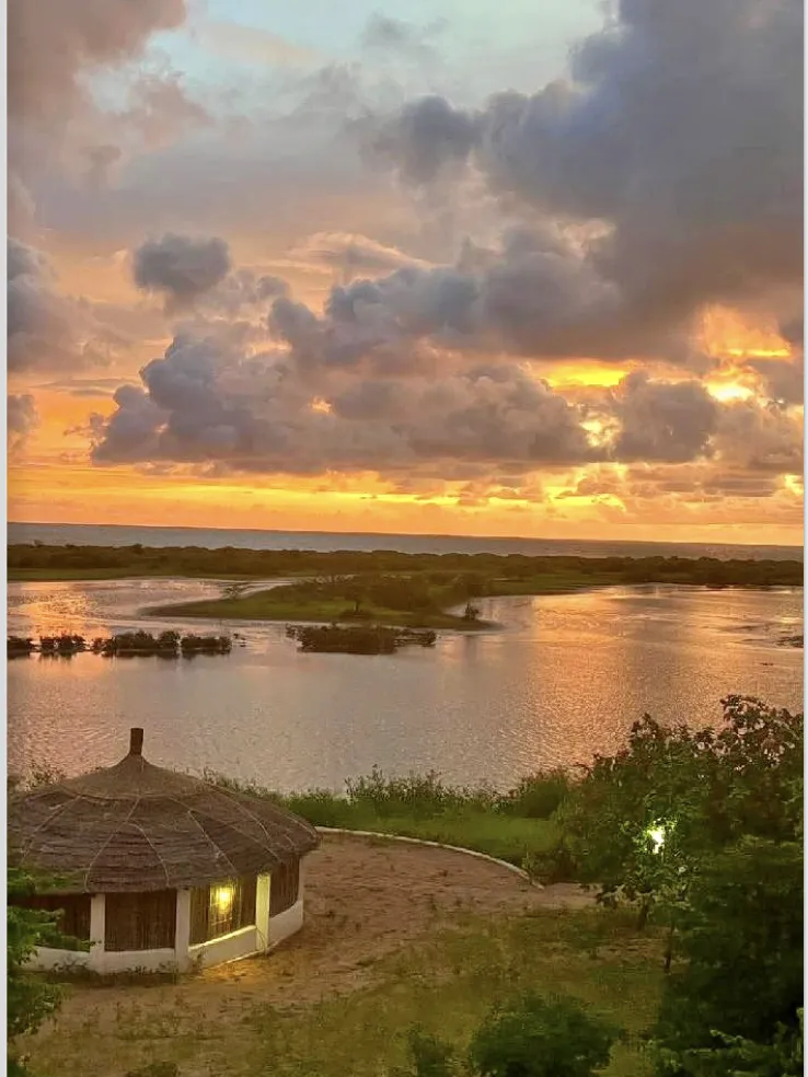 Superbe coucher de soleil embrasant le ciel au-dessus de la lagune et d'une case à Saly.